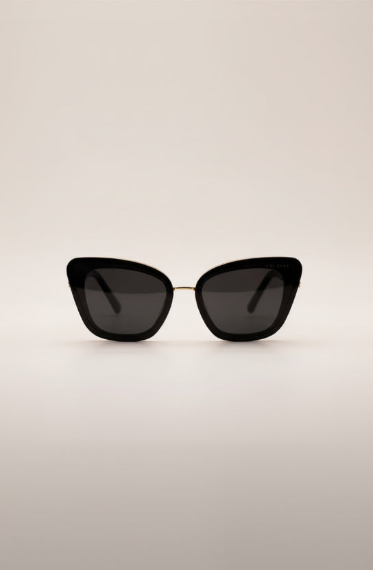 Sunglasses with gold frame and black lenses on a light beige background