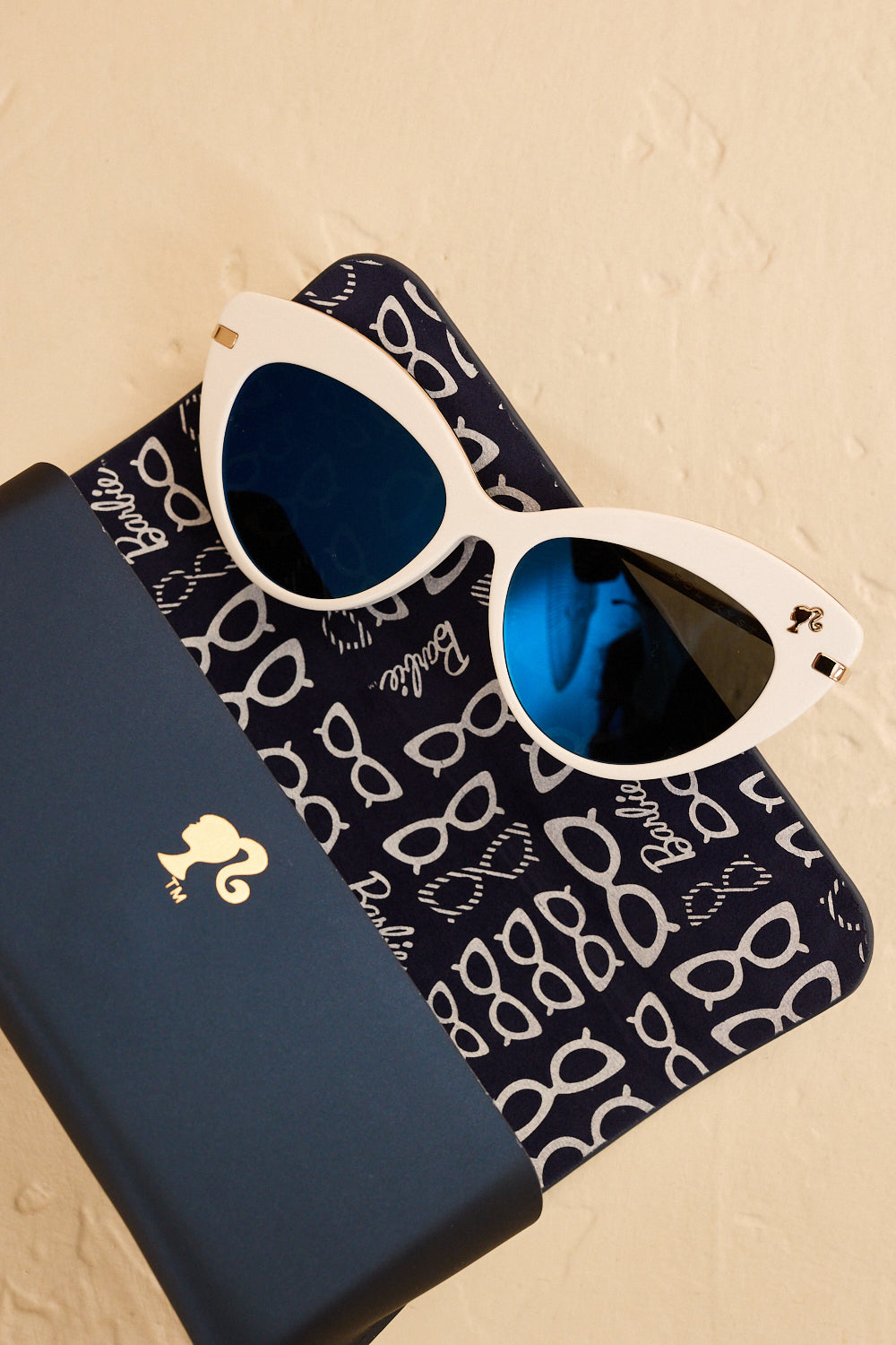 Barbie x Sol Kyst white cat-eye sunglasses with blue lenses, shown with a matching navy case.