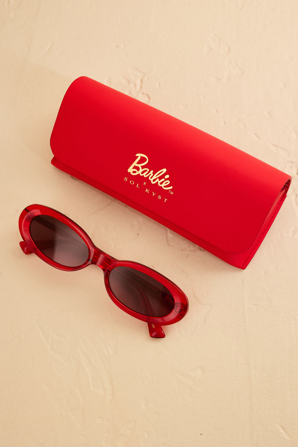 Barbie x Sol Kyst red oval sunglasses paired with a matching red protective case featuring gold branding.