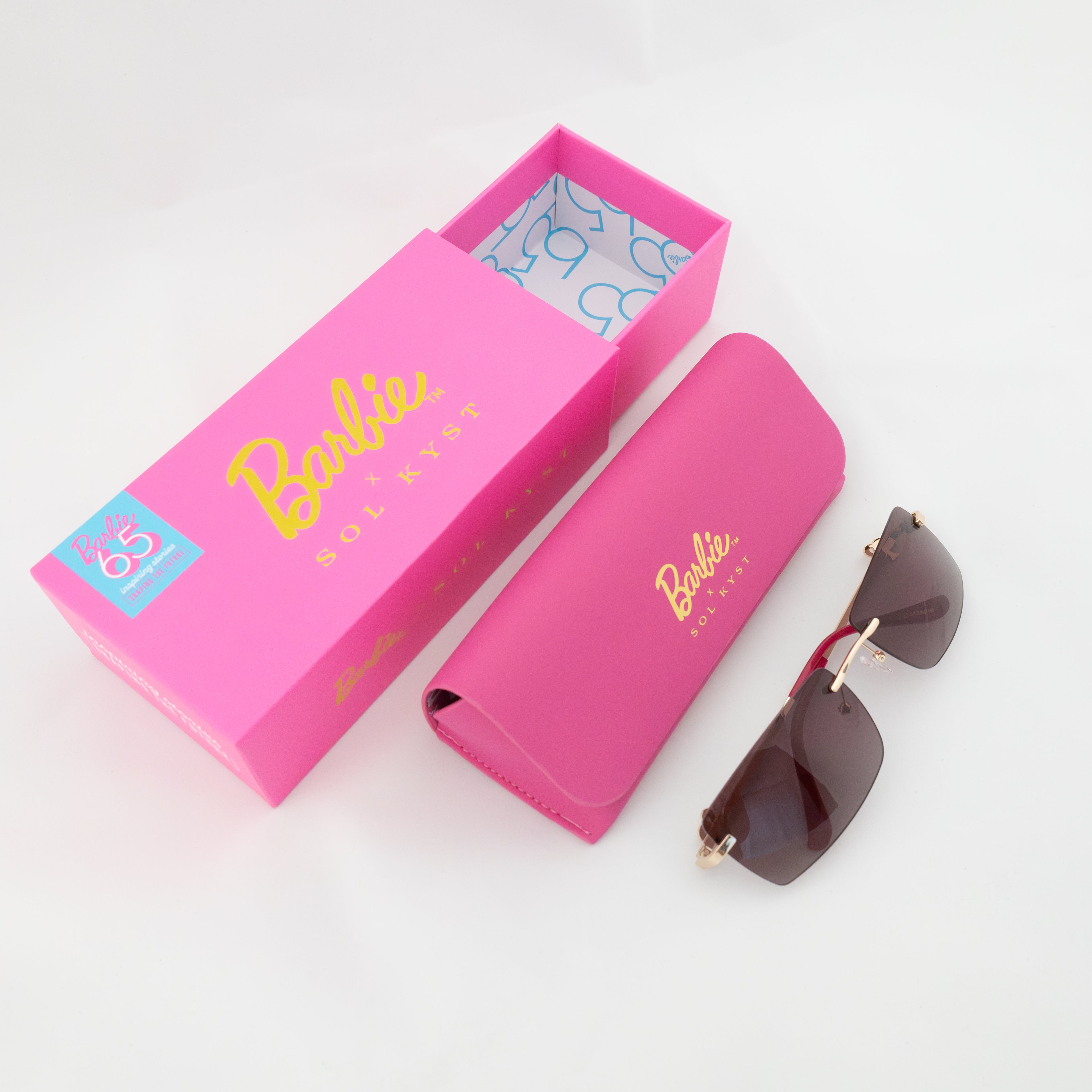 Barbie sunglasses with rose-tinted lenses, gold detailing, next to pink branded packaging.