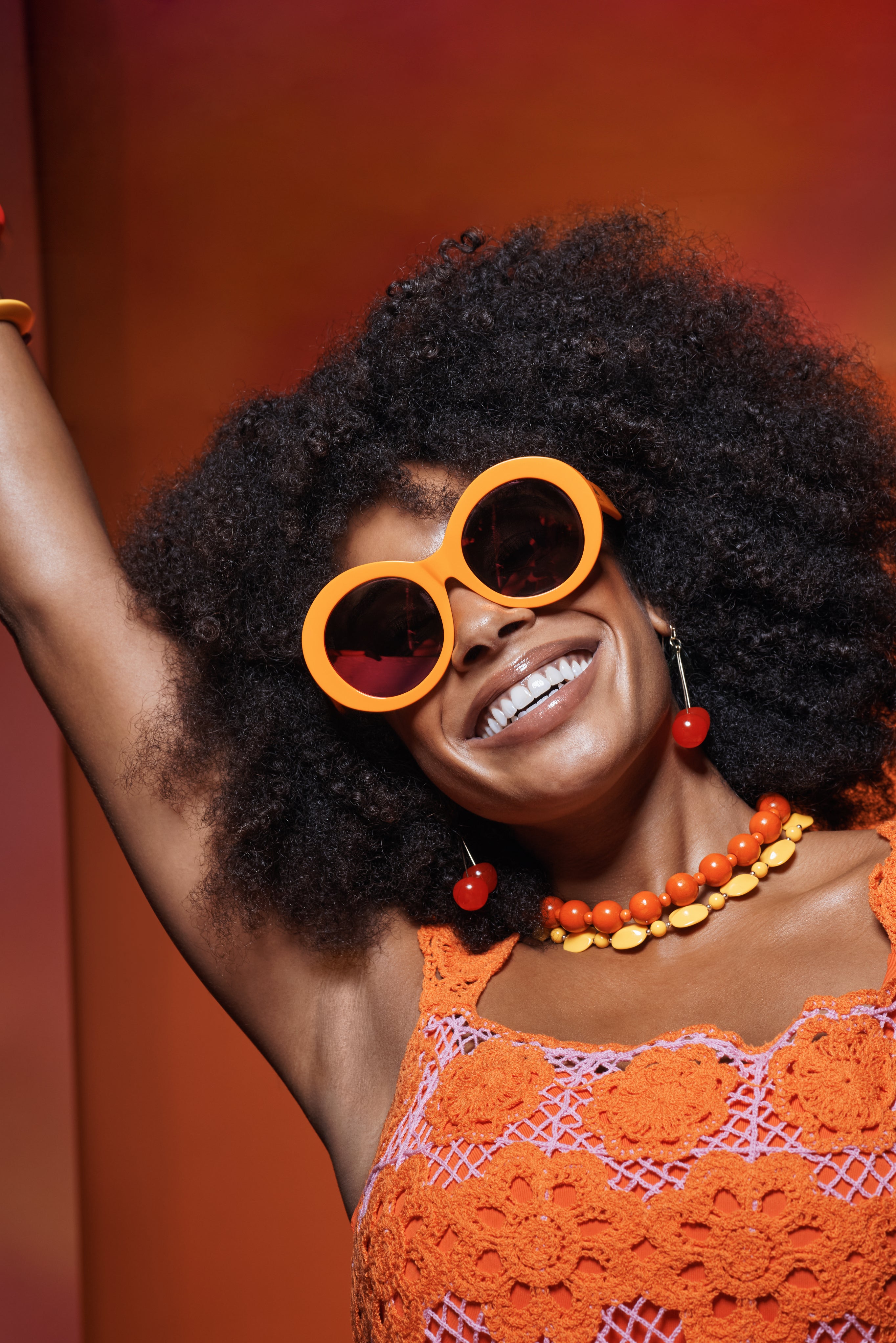 Model wearing Sol Kyst round sunglasses with orange frame, with matching dress and accessories.