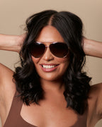 Woman wearing a brown tank top and sunglasses with a beige background