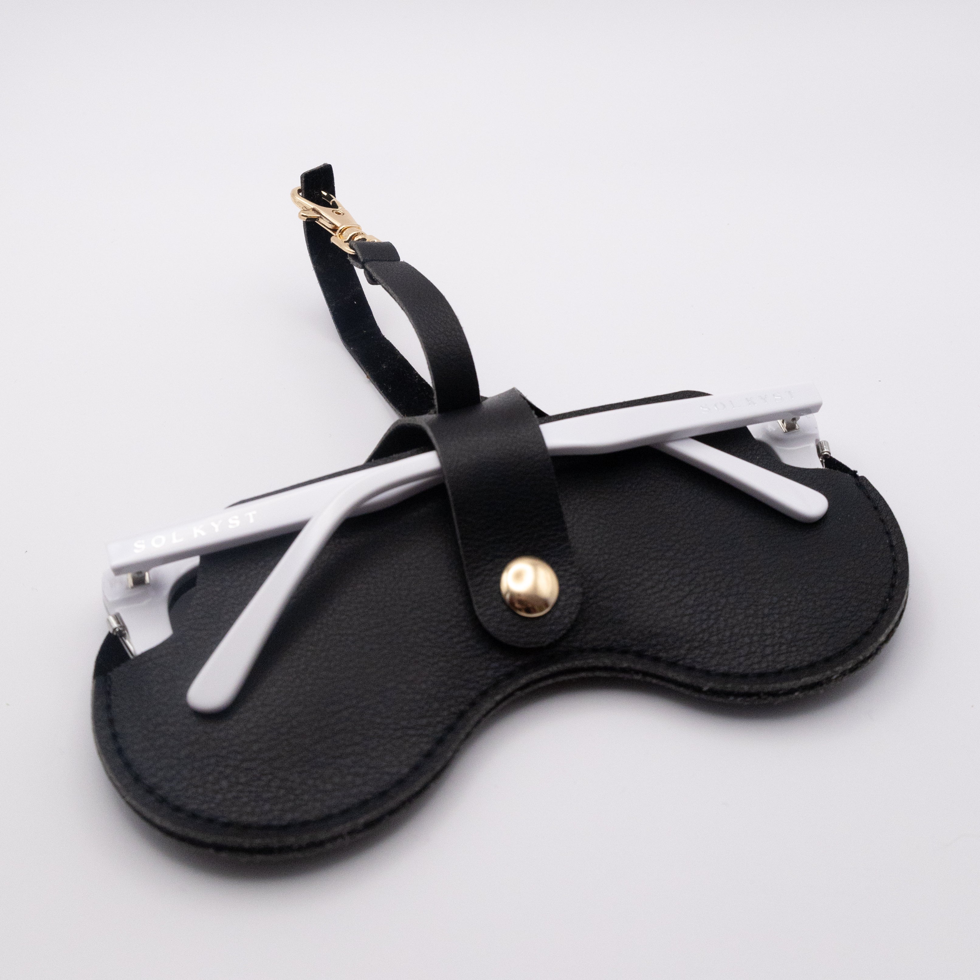 Back view of black Sol Kyst "Kyst Klip" holding sunglasses with white frames on a white background.