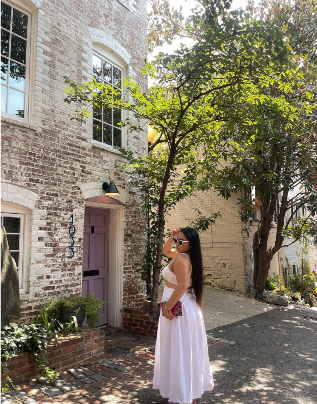 Model standing in the road in front of a house, wearing a white dress and matching white Sol Kyst cat eye sunglasses.