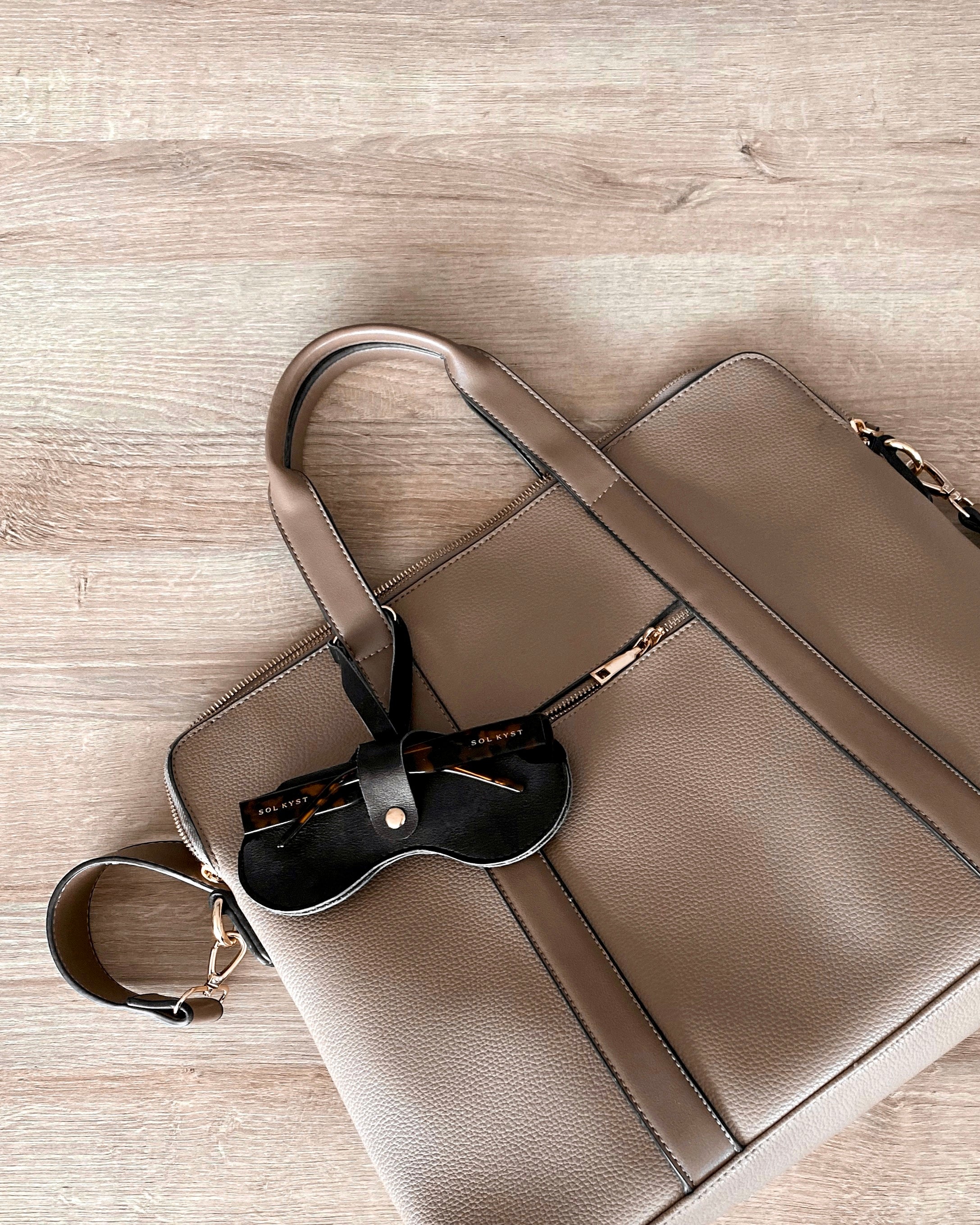 Back view of black Sol Kyst "Kyst Klip" holding tortoise glasses, attached to a beige handbag.