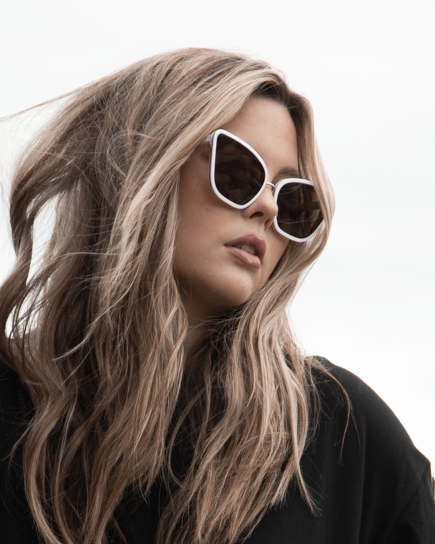 Model with blonde hair wearing Sol Kyst cat eye sunglasses and a black sweater, in front of a white background.